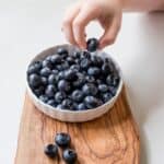 person holding bowl of black berries