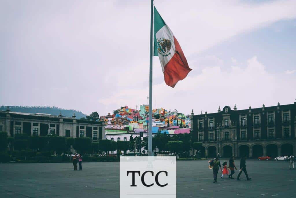 Colorful cityscape of Toluca with large Mexican flag in the foreground, vibrant buildings in the backdrop.